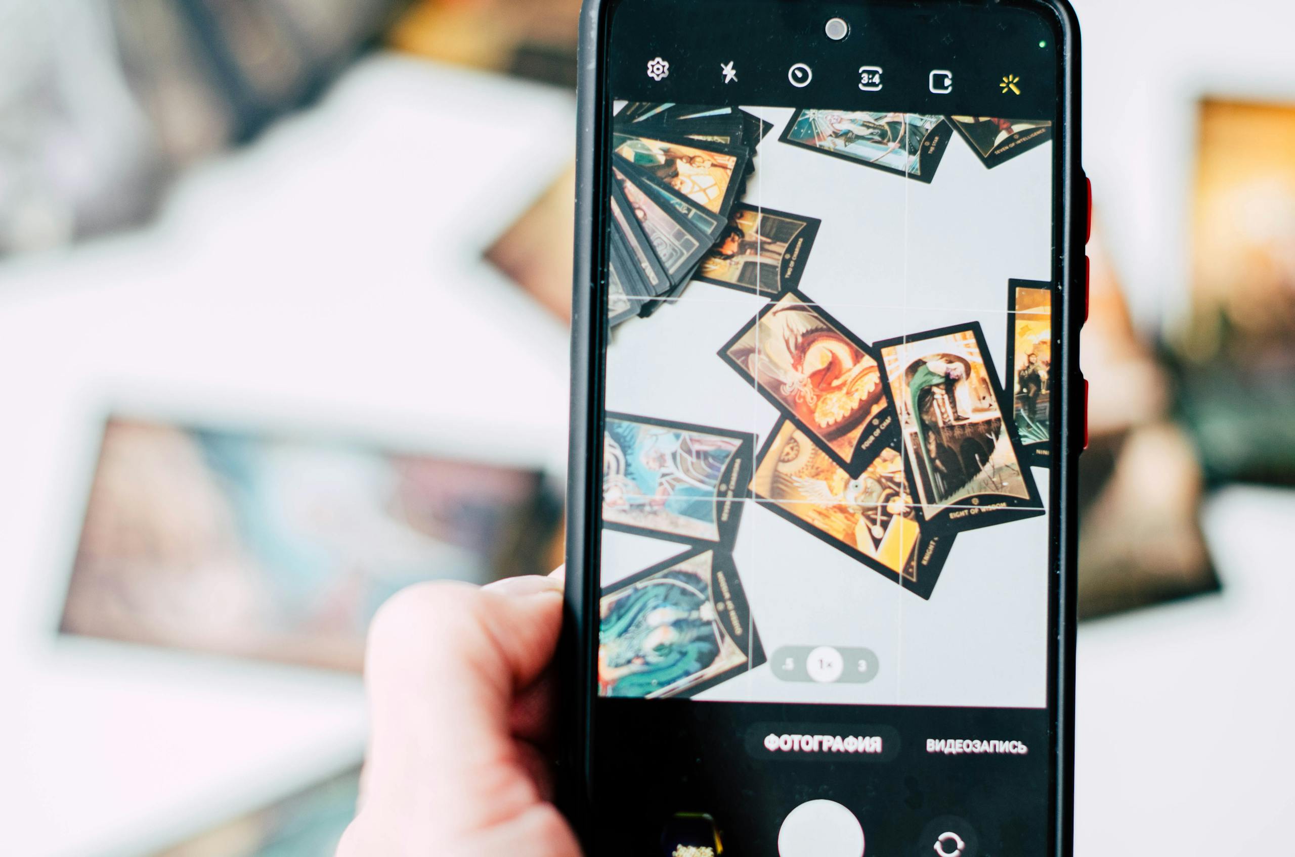 Hand holding smartphone capturing colorful tarot cards in focus.